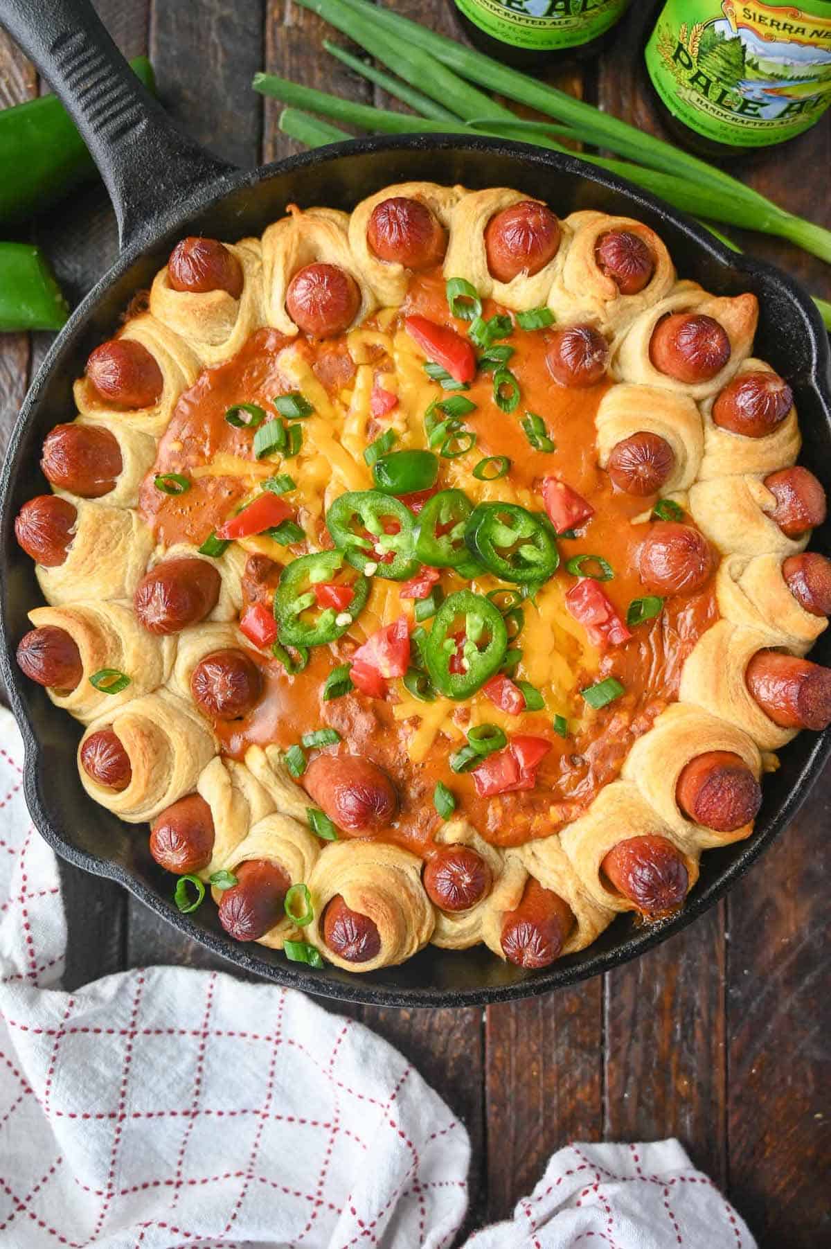 A cast iron skillet with wrapped mini hotdogs and a chili dip in the middle.