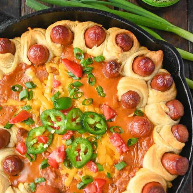 A cast iron skillet with wrapped mini hotdogs and a chili dip in the middle.
