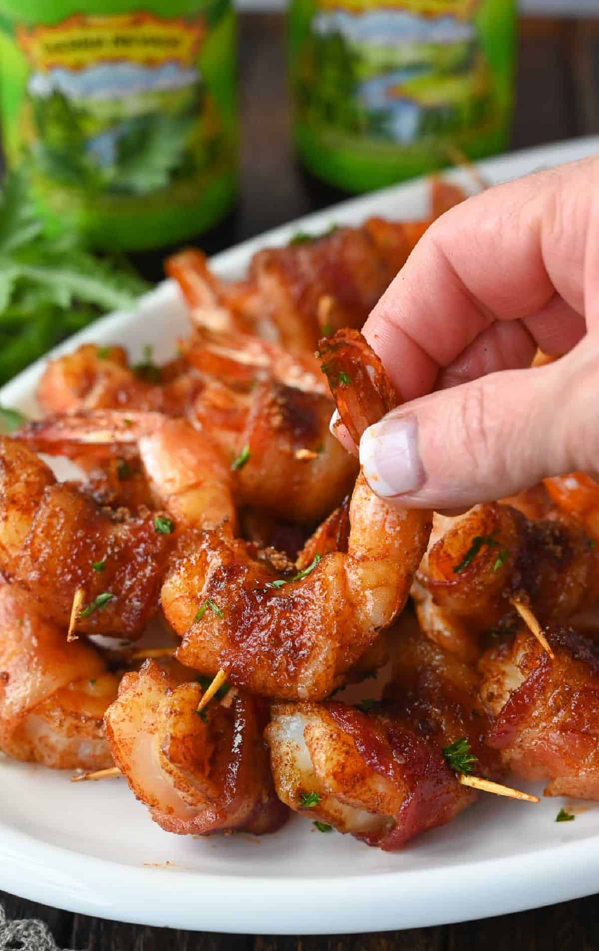 Bacon wrapped shrimp on a plate and one being grabbed.