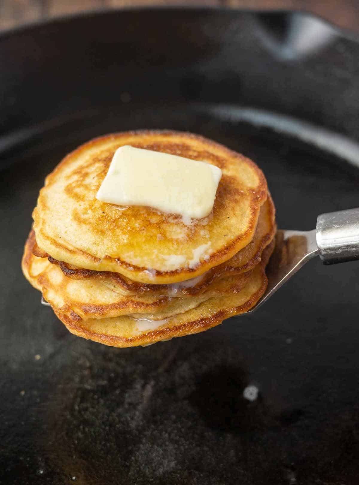 Hoe cakes stacked on top of a spatulawith a pat of butter on top.