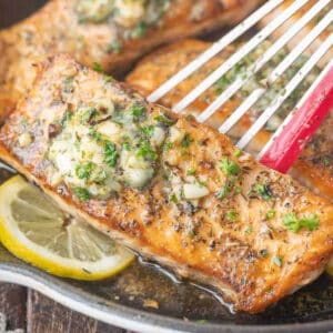 A spatula picking up a salmon filet out of a skillet.