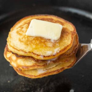 Hoe cakes stacked on top of a spatulawith a pat of butter on top.
