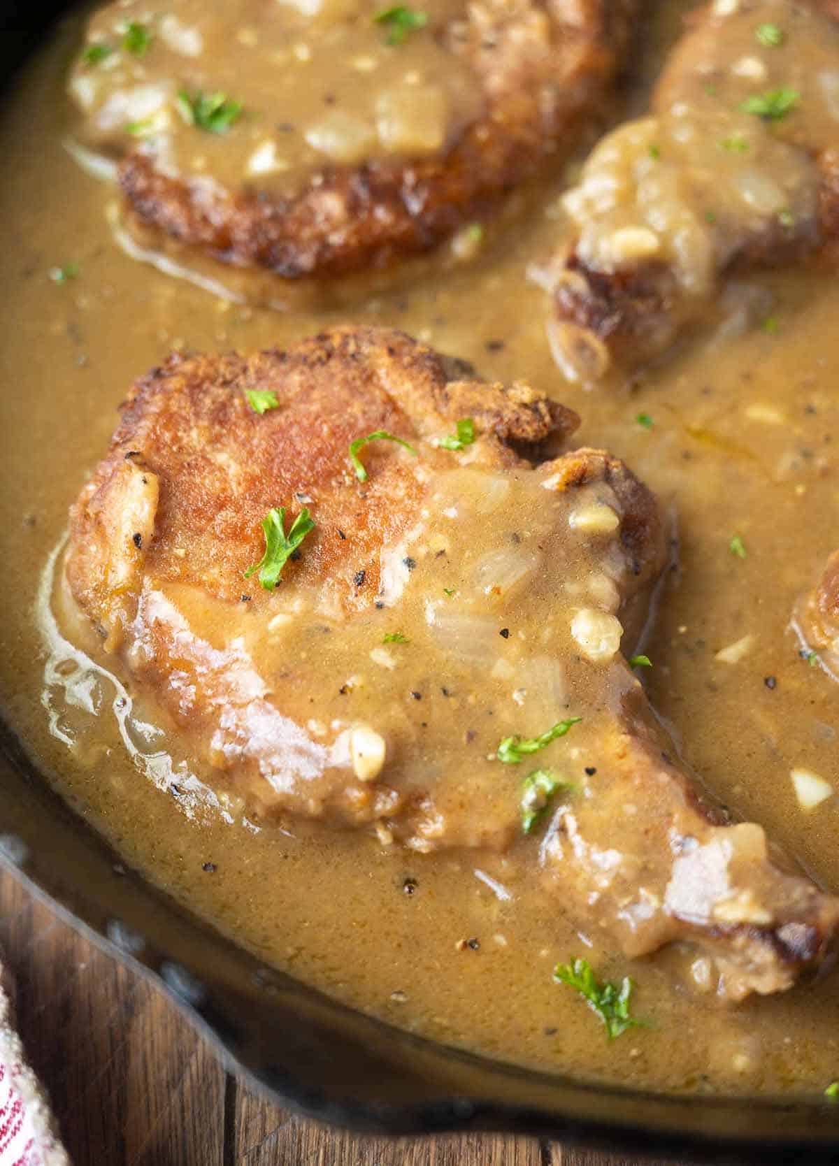 Pork chops smothered in a gravy in a skillet.