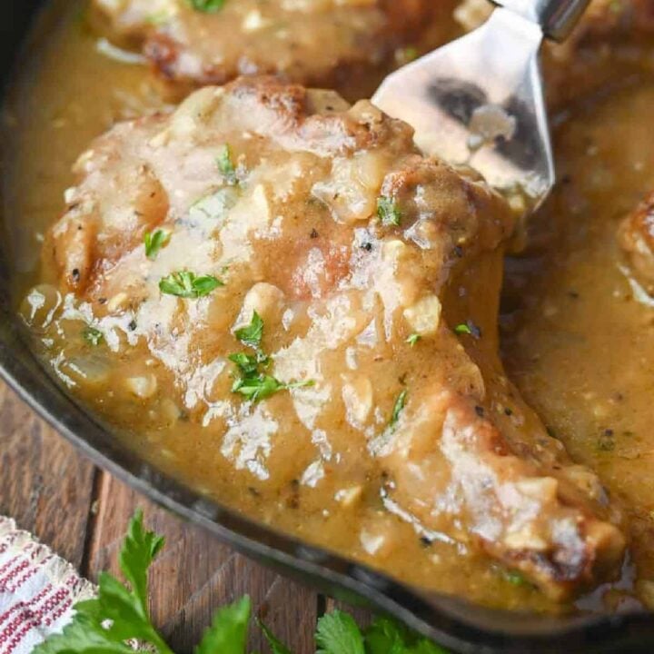 Pork chops smothered in a gravy in a skillet.