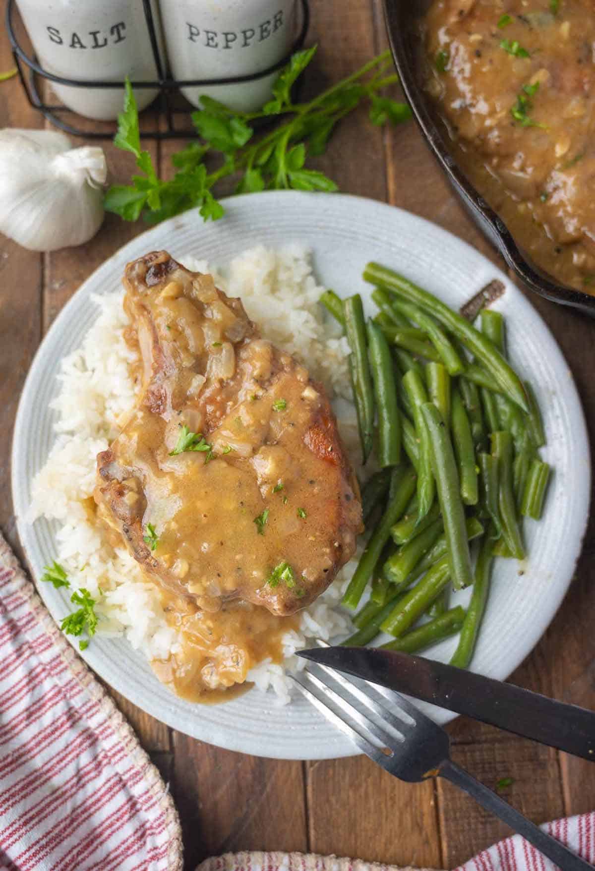 Smothered pork chop placed on some white rice with green beans.