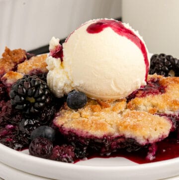 Southern berry cobbler served on a white plate with a scoop of ice cream on top.