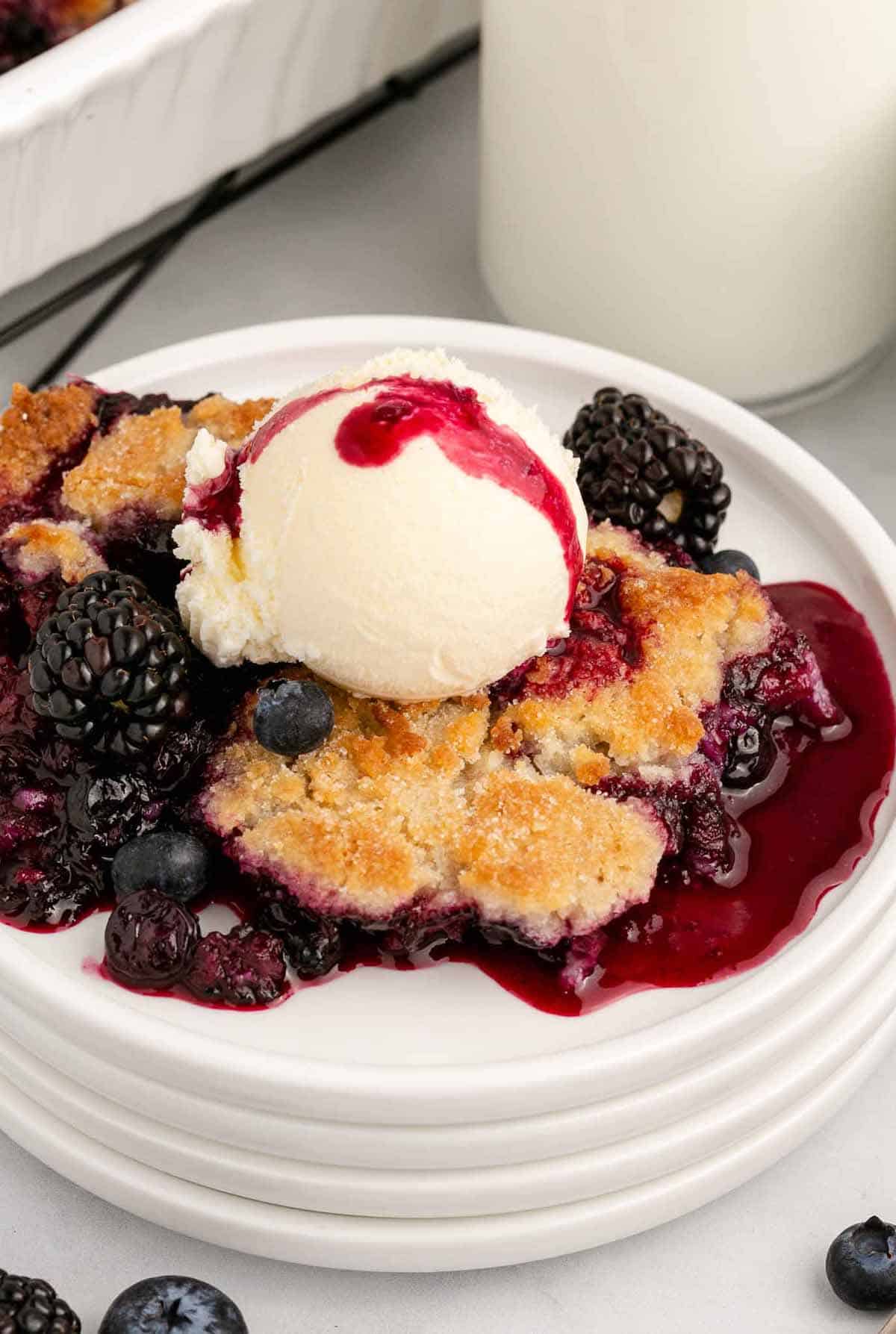 Southern berry cobbler served on a white plate with a scoop of ice cream on top.