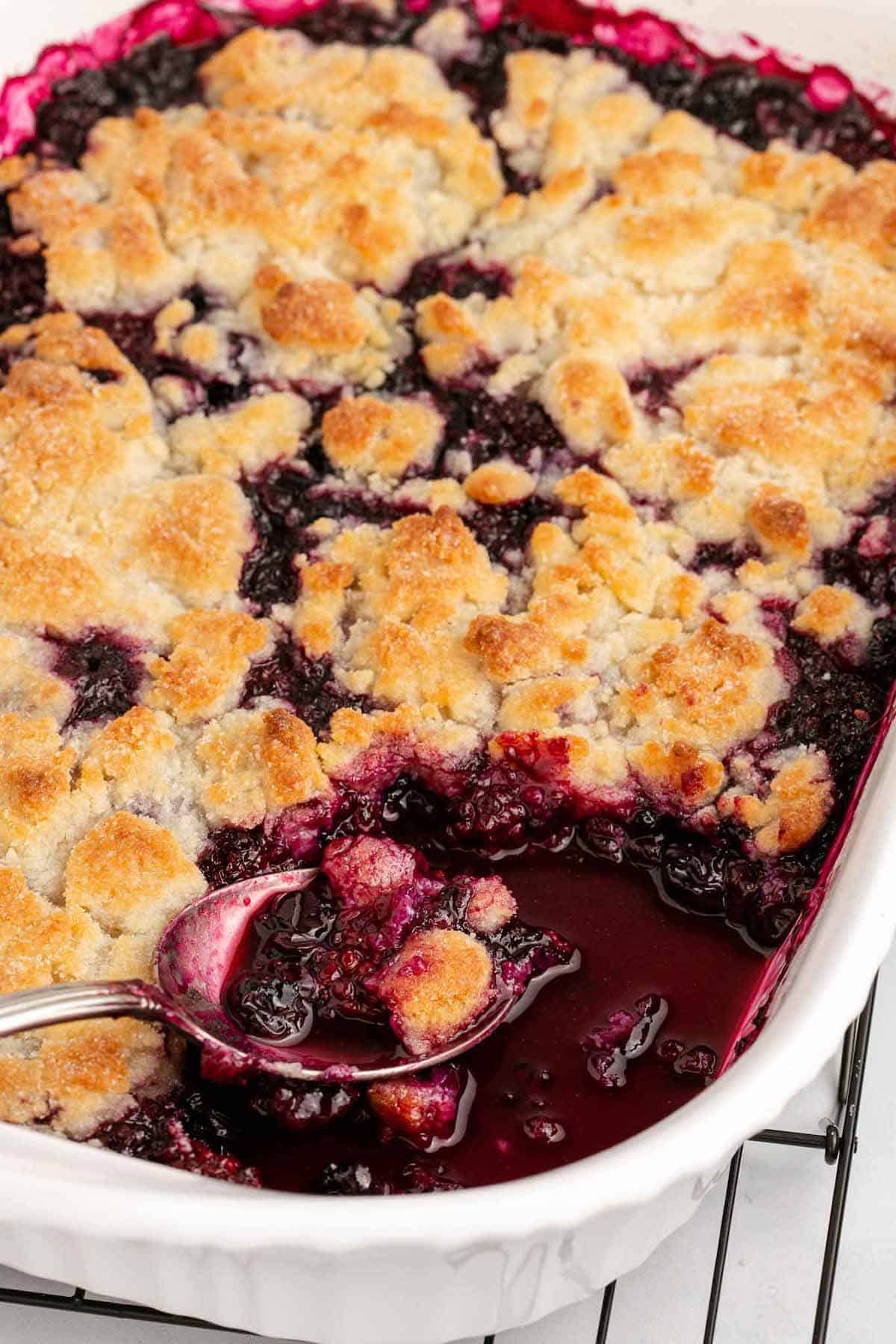 Fruit cobbler in a baking dish with a spoon scooping some out.