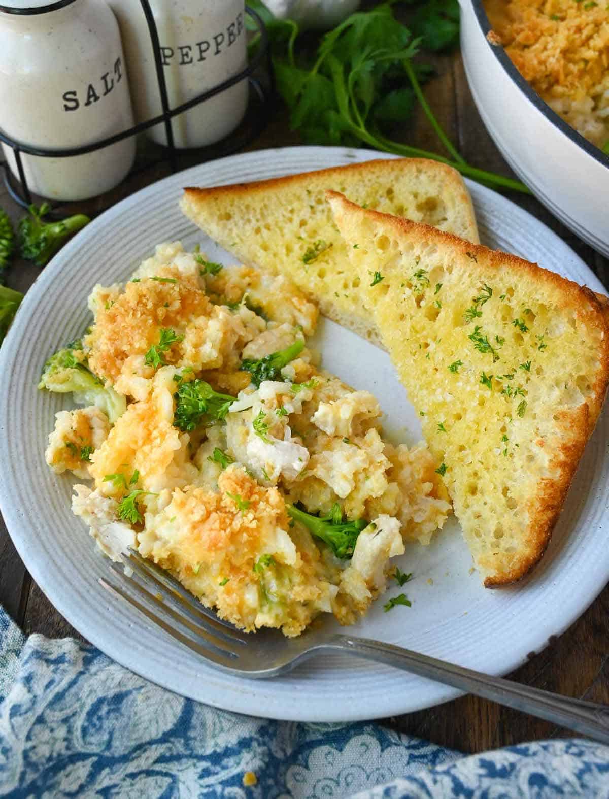 A serving of chicken broccoli casserole on a plate with a side of garlic bread.