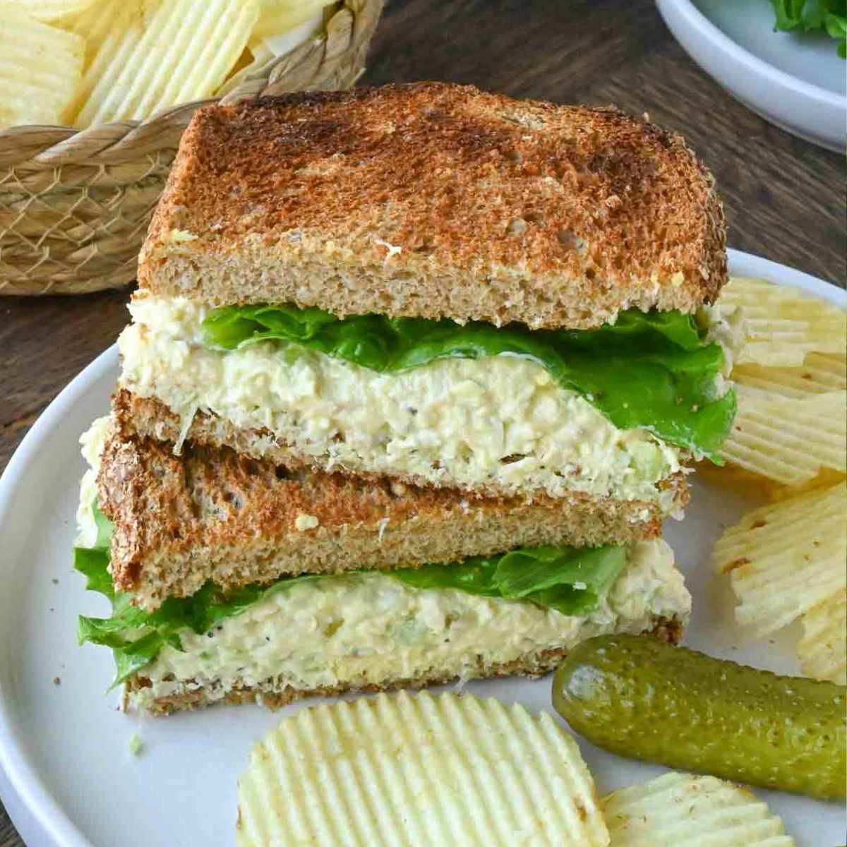 A halved chick fil a chicken salad sandwich on a plate with chips and a pickle.