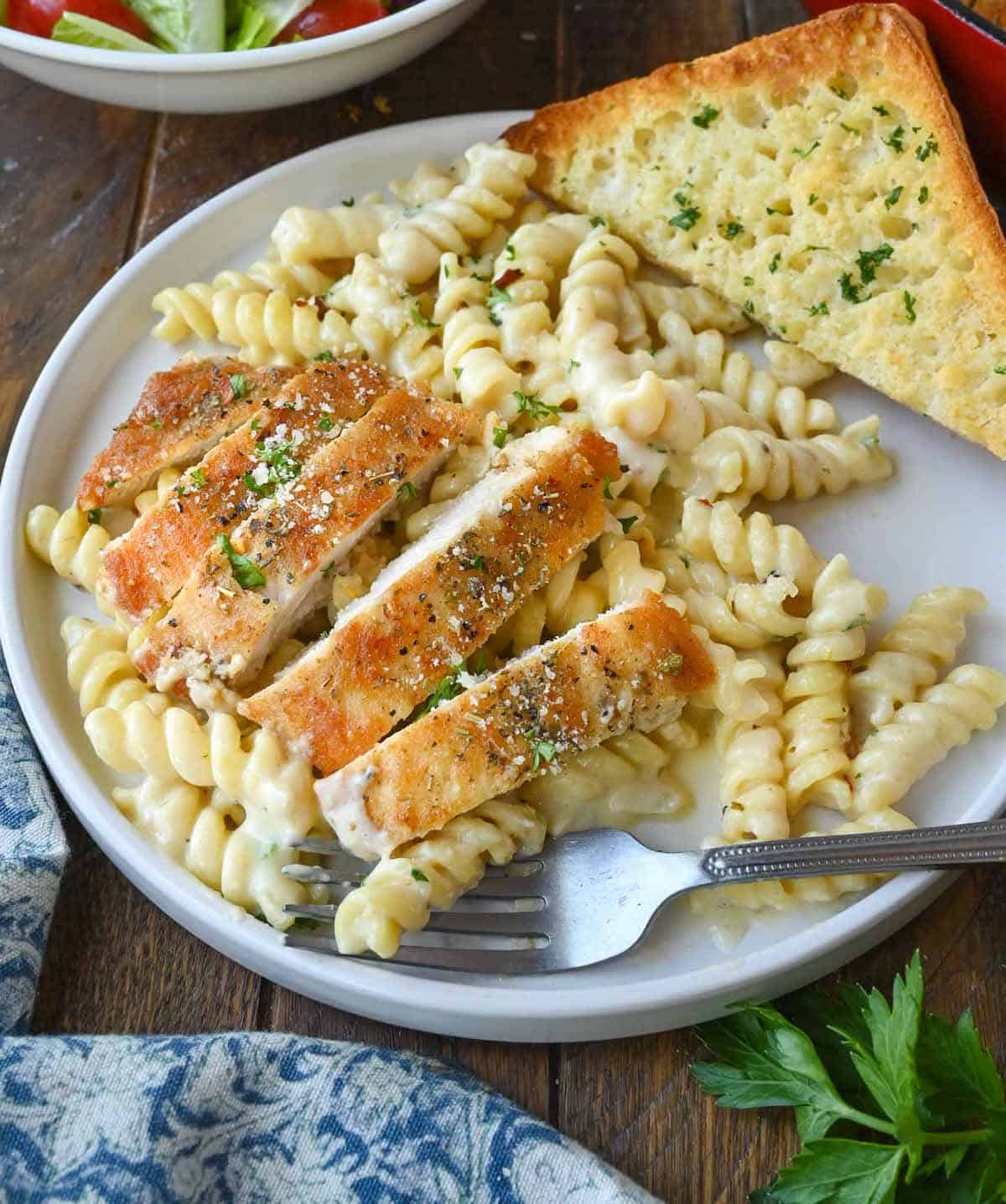 Chicken and pasta on a plate with garlic bread.