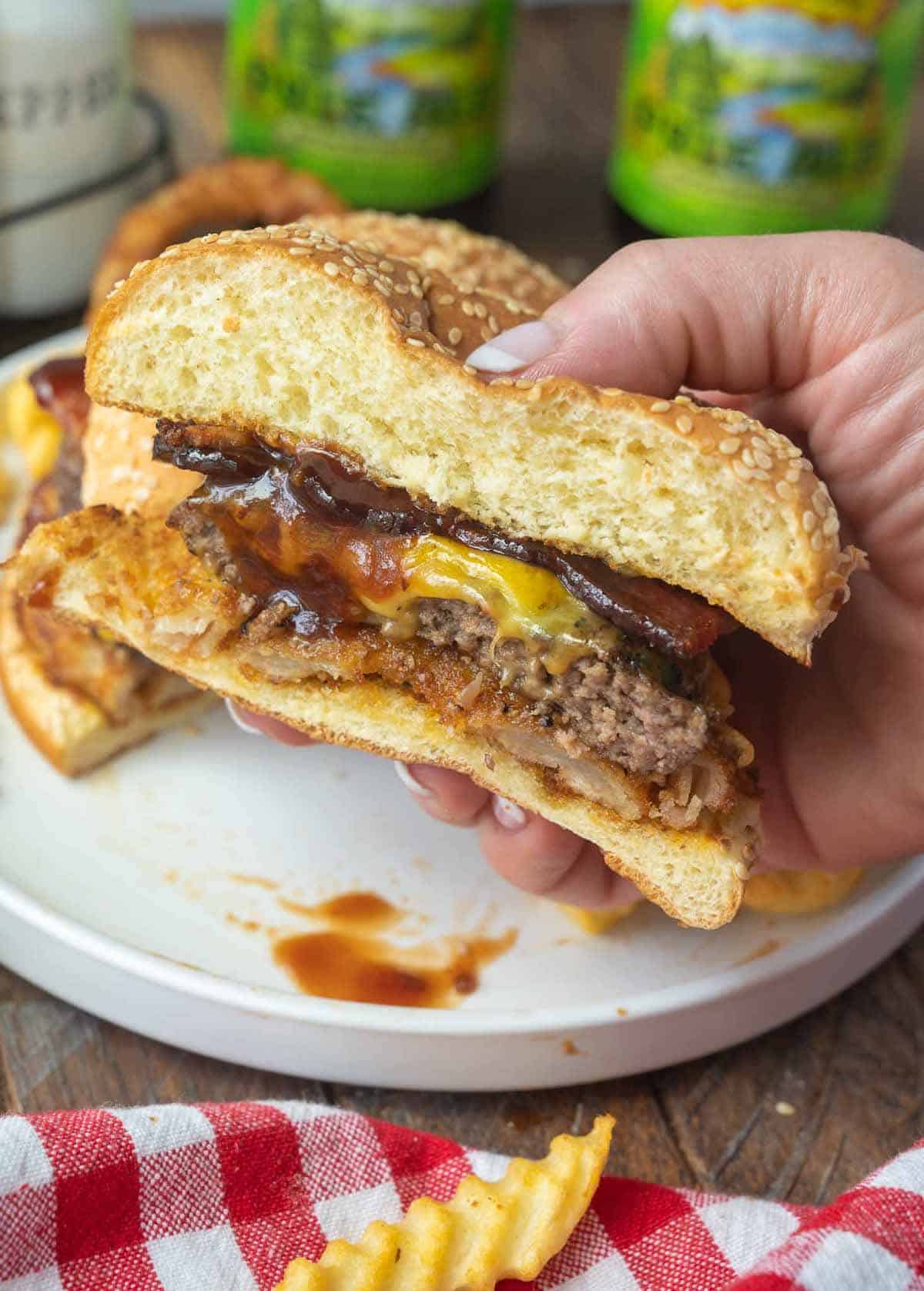 A bacon cheeseburger cut in half and held in a hand.