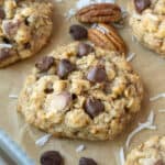 Cowboy cookies on a bking sheet with pecans and chocolate chips on the side.