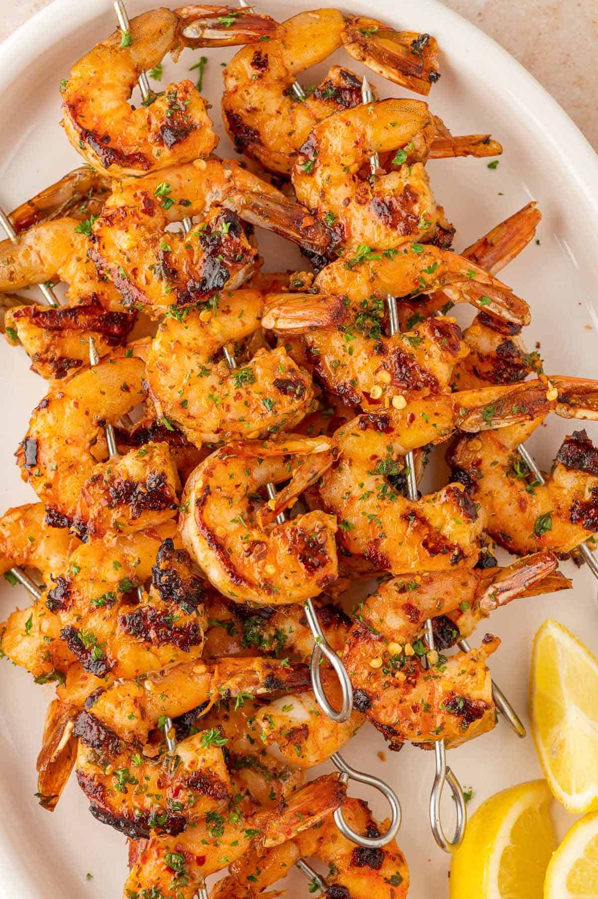 Grilled shrimp skewers on a white platter with lemon wedges.
