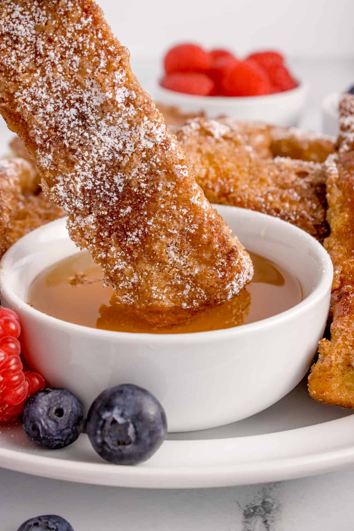A french toast stick being dipped into a cup of syrup.