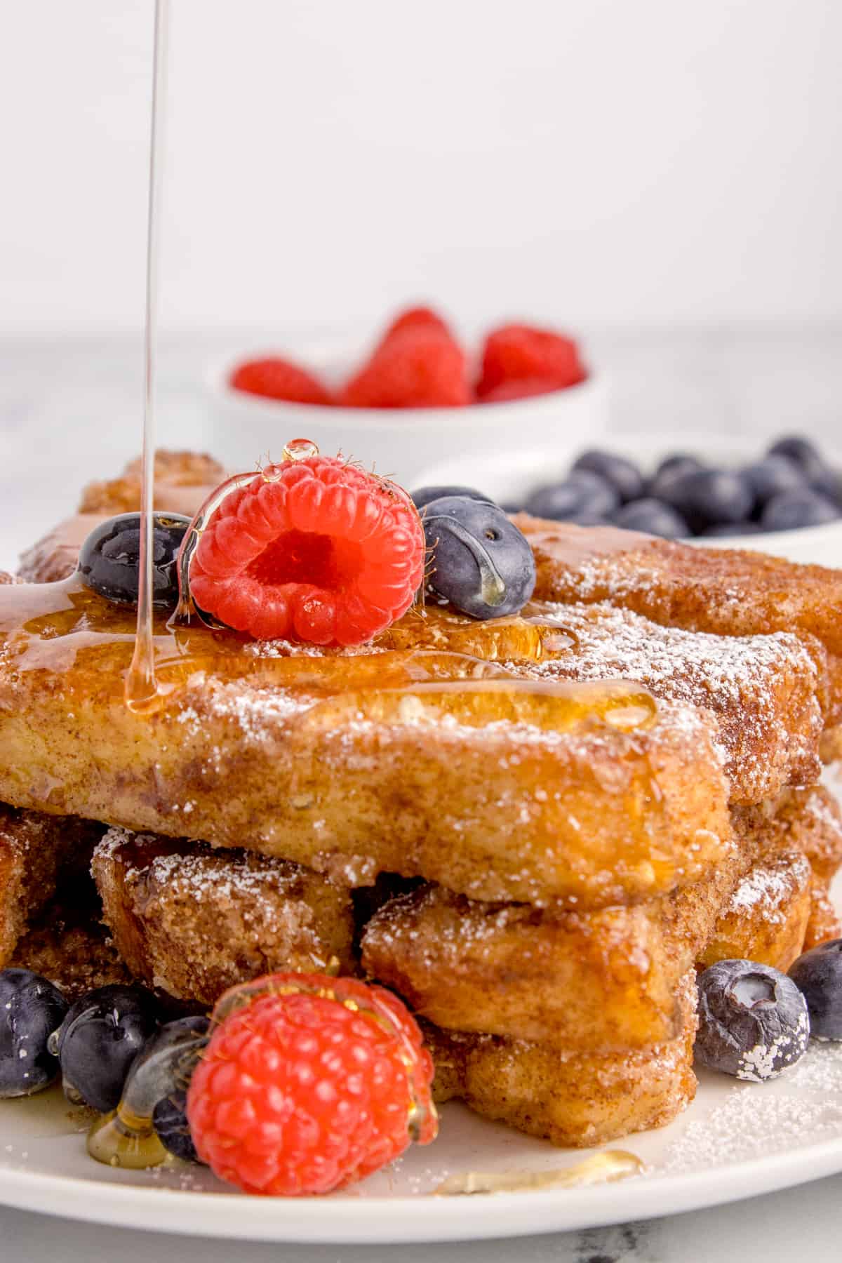 French toast sticks on a plate with syrup being drizzled on top.