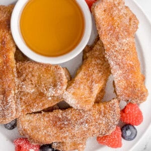 A plate of french toast sticks and syrup.