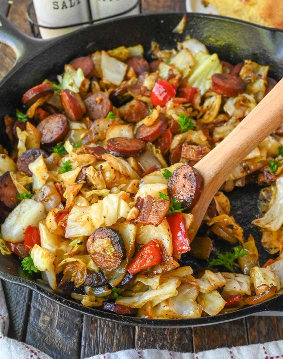 A wooden spoon scooping up a serving of fried cabbage and sausage.
