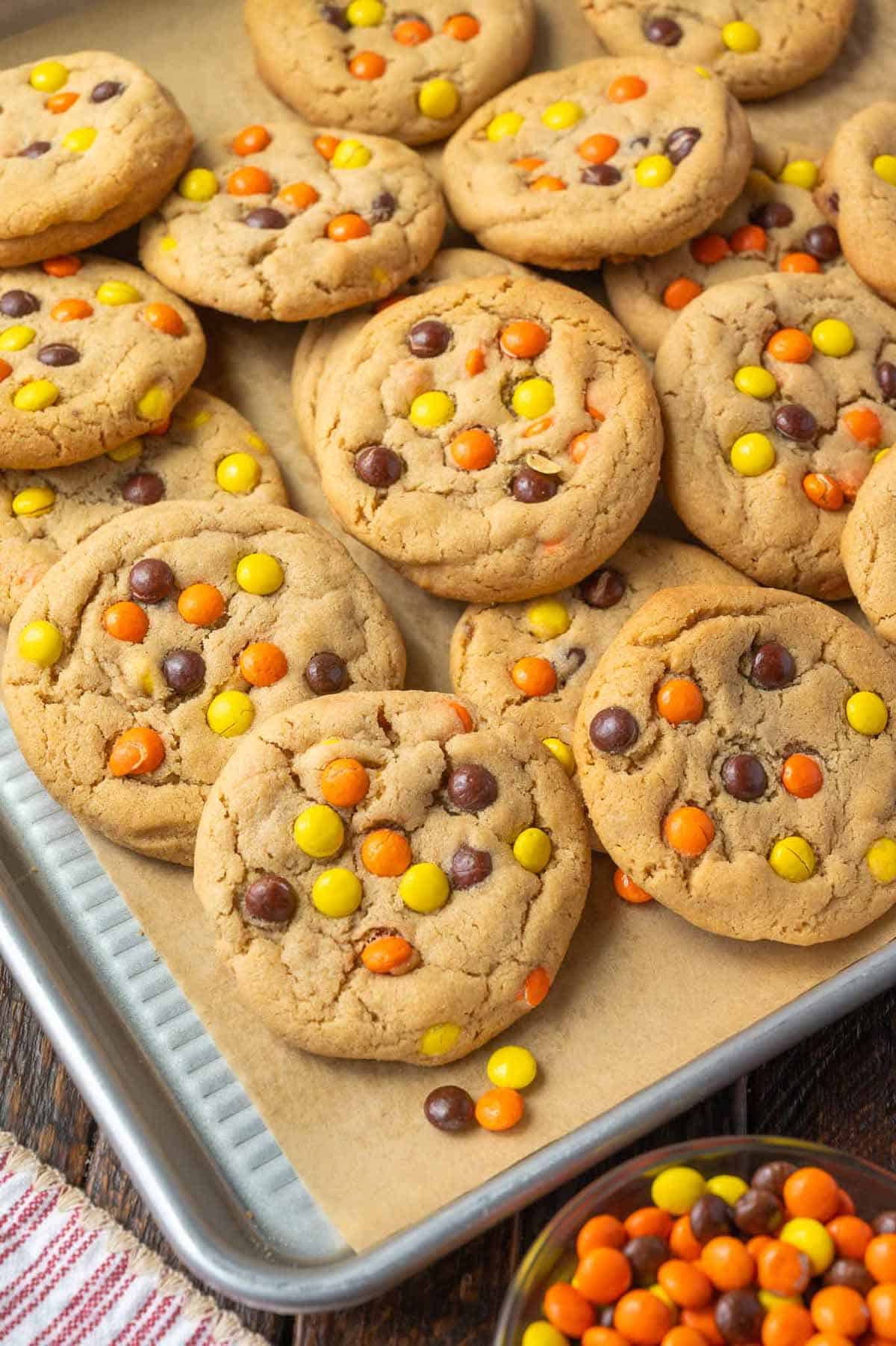 A pile of baked Reese's pieces peanut butter cookies on a baking sheet.