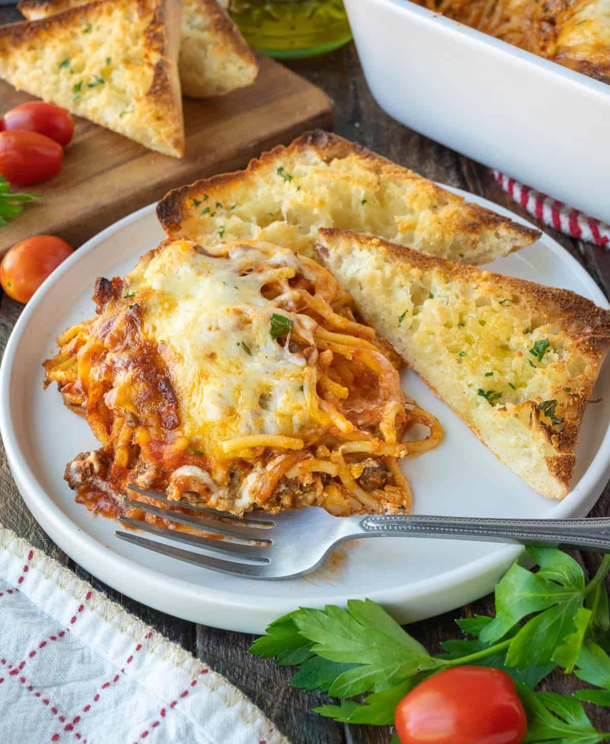 Baked spaghetti placed on a plate with garlic bread.