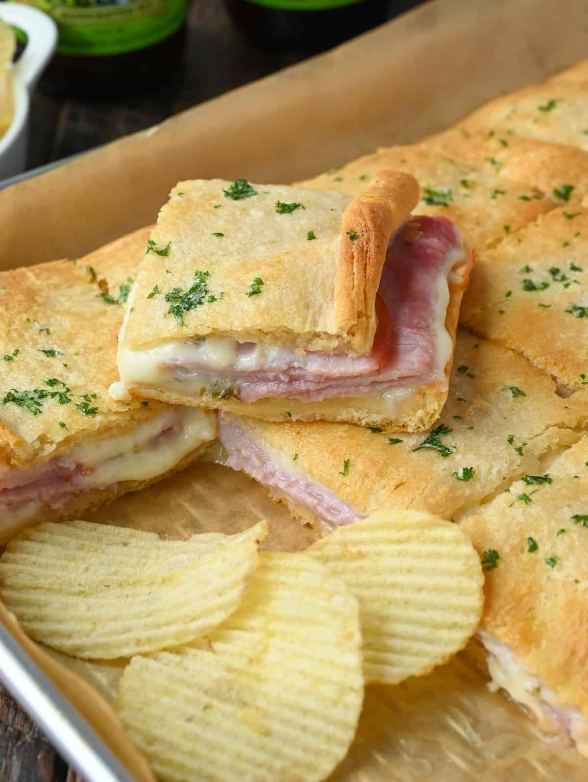 Hot ham ans cheese sandwich square placed on top of another one and some potato chips.