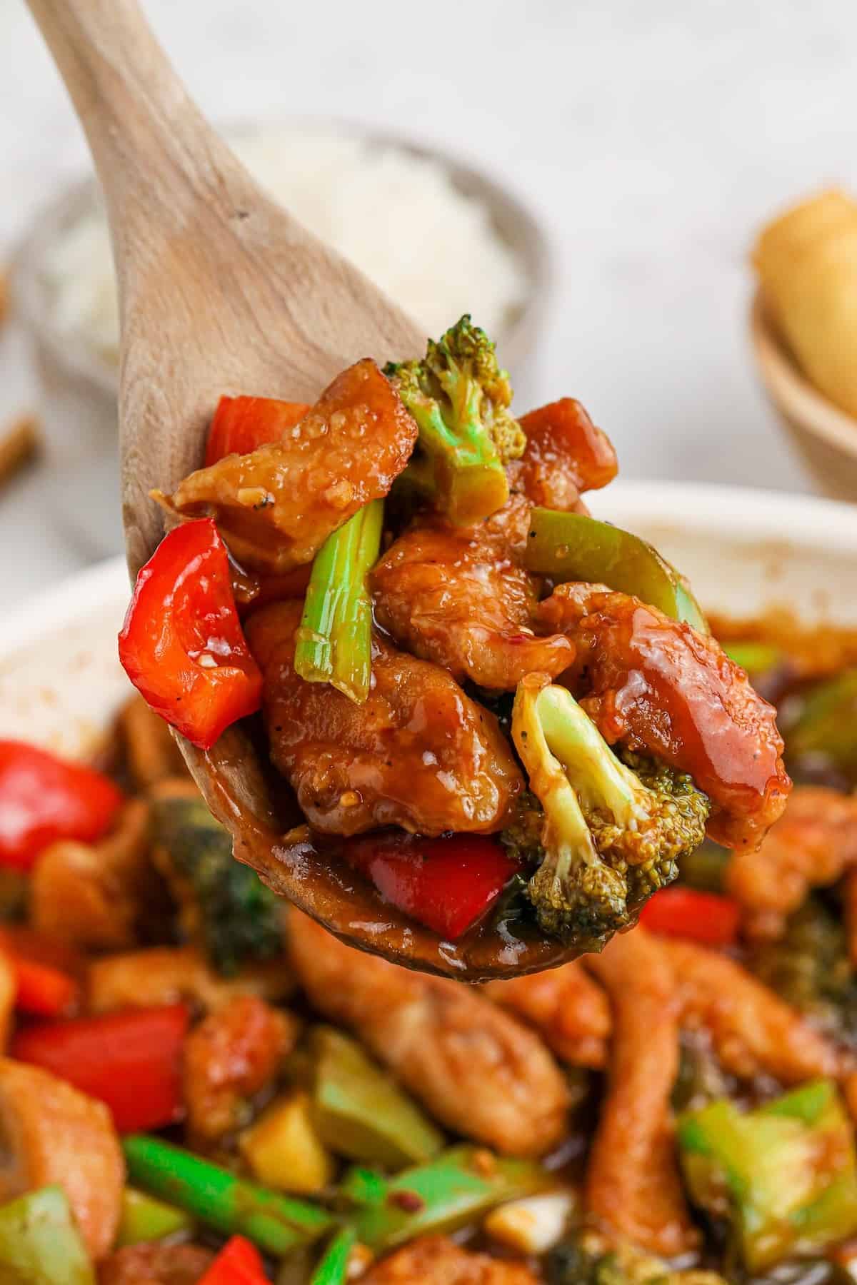 A close up of a wooden spoon scooping up spicy hunan chicken.