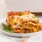 A fork sitting beside a plate of Meat Lovers Lasagna on a countertop.