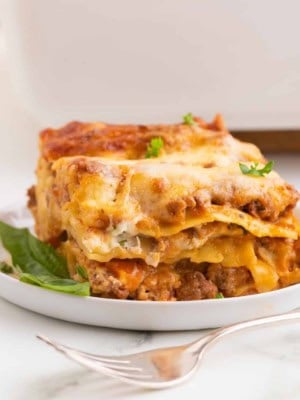 A fork sitting beside a plate of Meat Lovers Lasagna on a countertop.