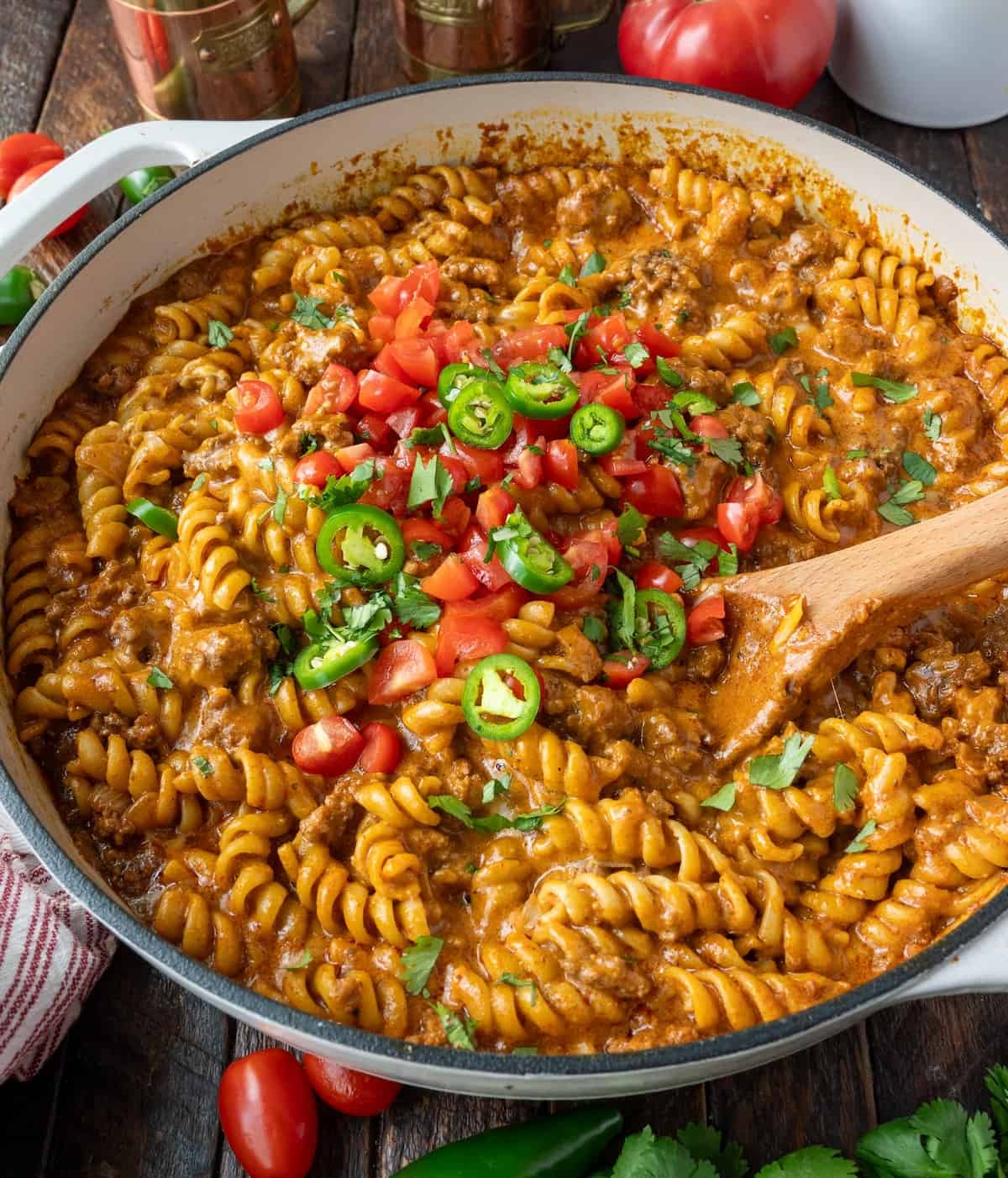 A wooden spoon stirring a skillet of one pot enchilada pasta on the stove top.