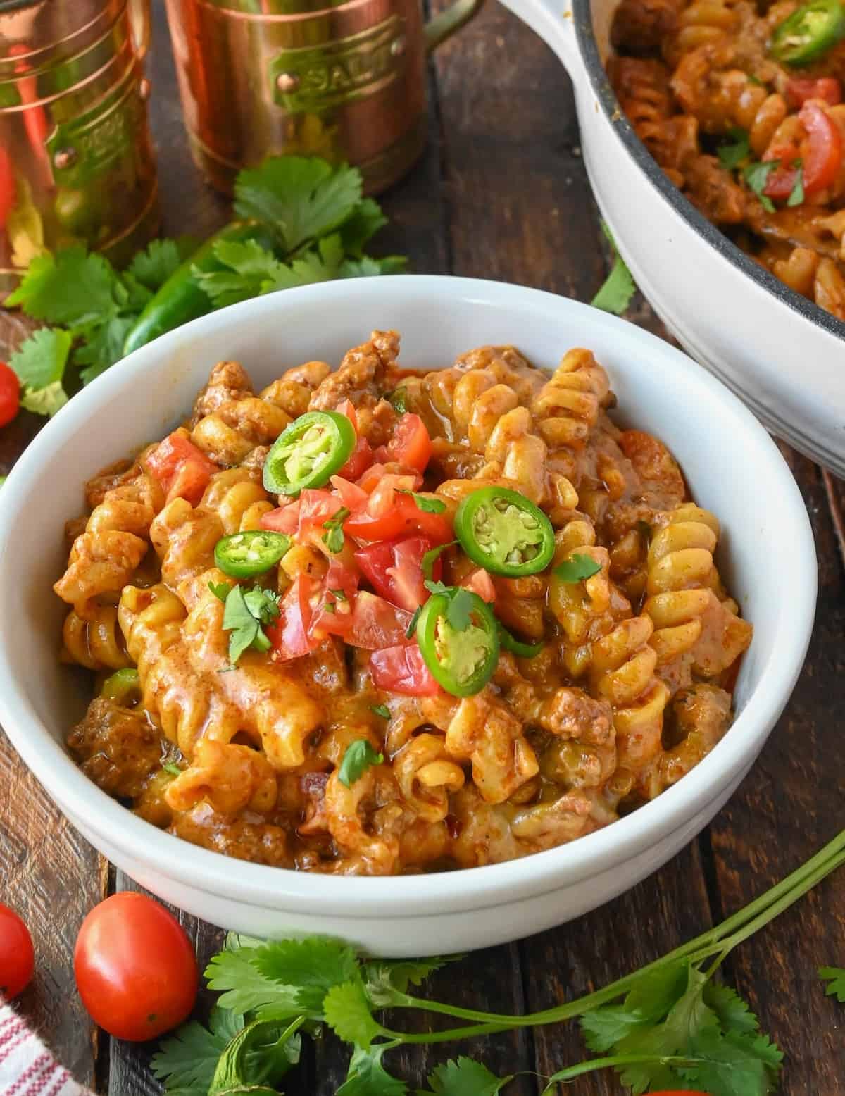 A bowl of one pot enchilada pasta sitting next to a pot.