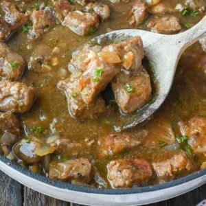 A wooden spoon scooping out some beef tips and gravy.