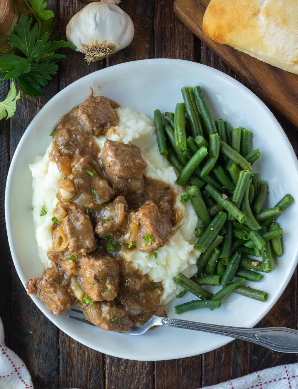 Beef tips and gravy served with mashed potatoes and green beans.