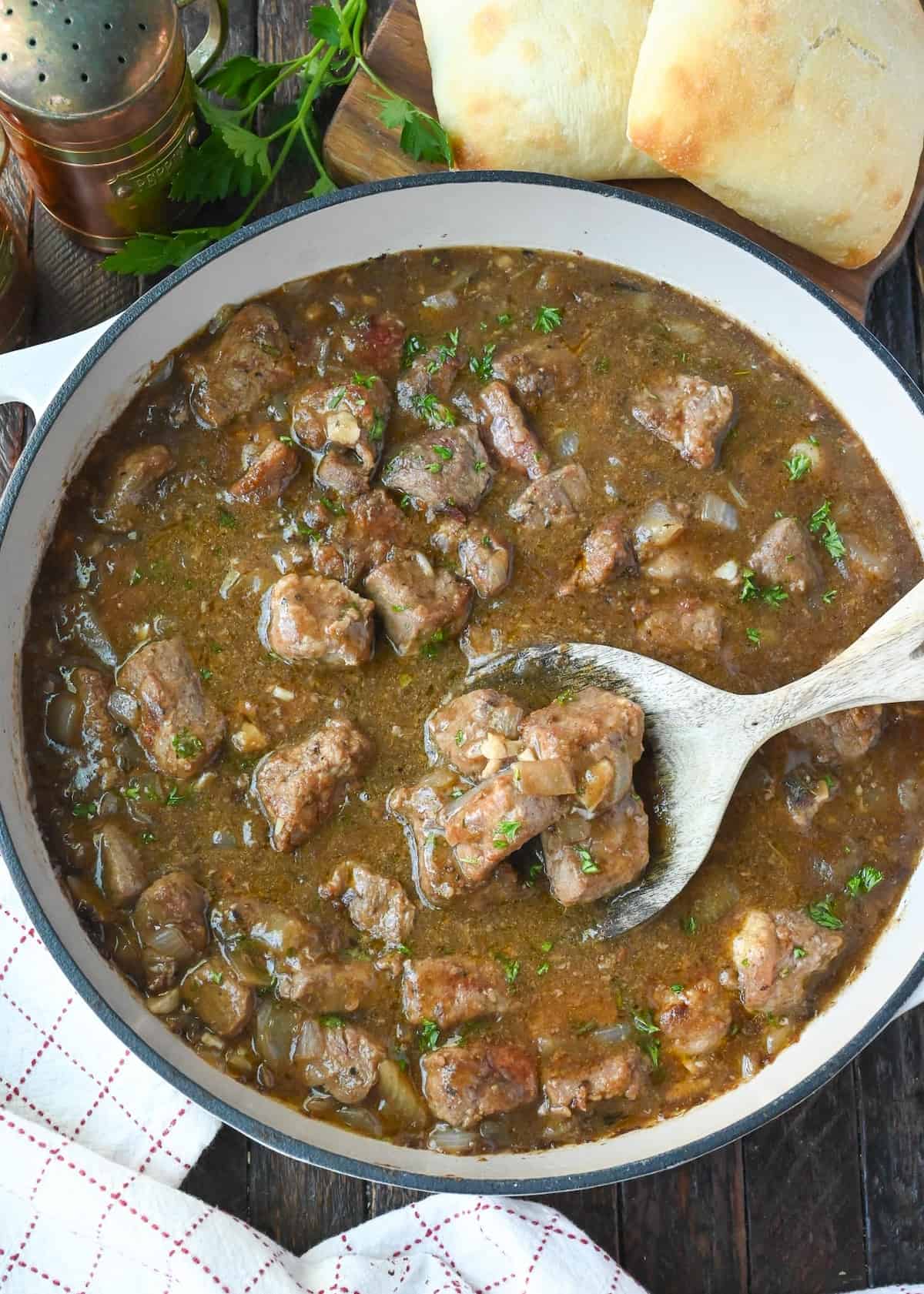 A wooden spoon scooping out some beef tips and gravy.