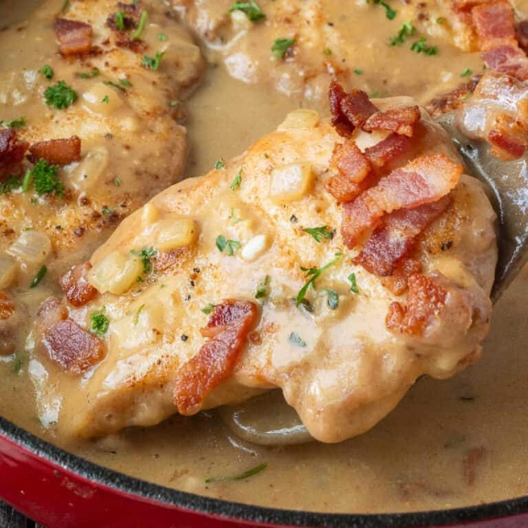 A spatula picking of a piece of chicken breast from a skillet.