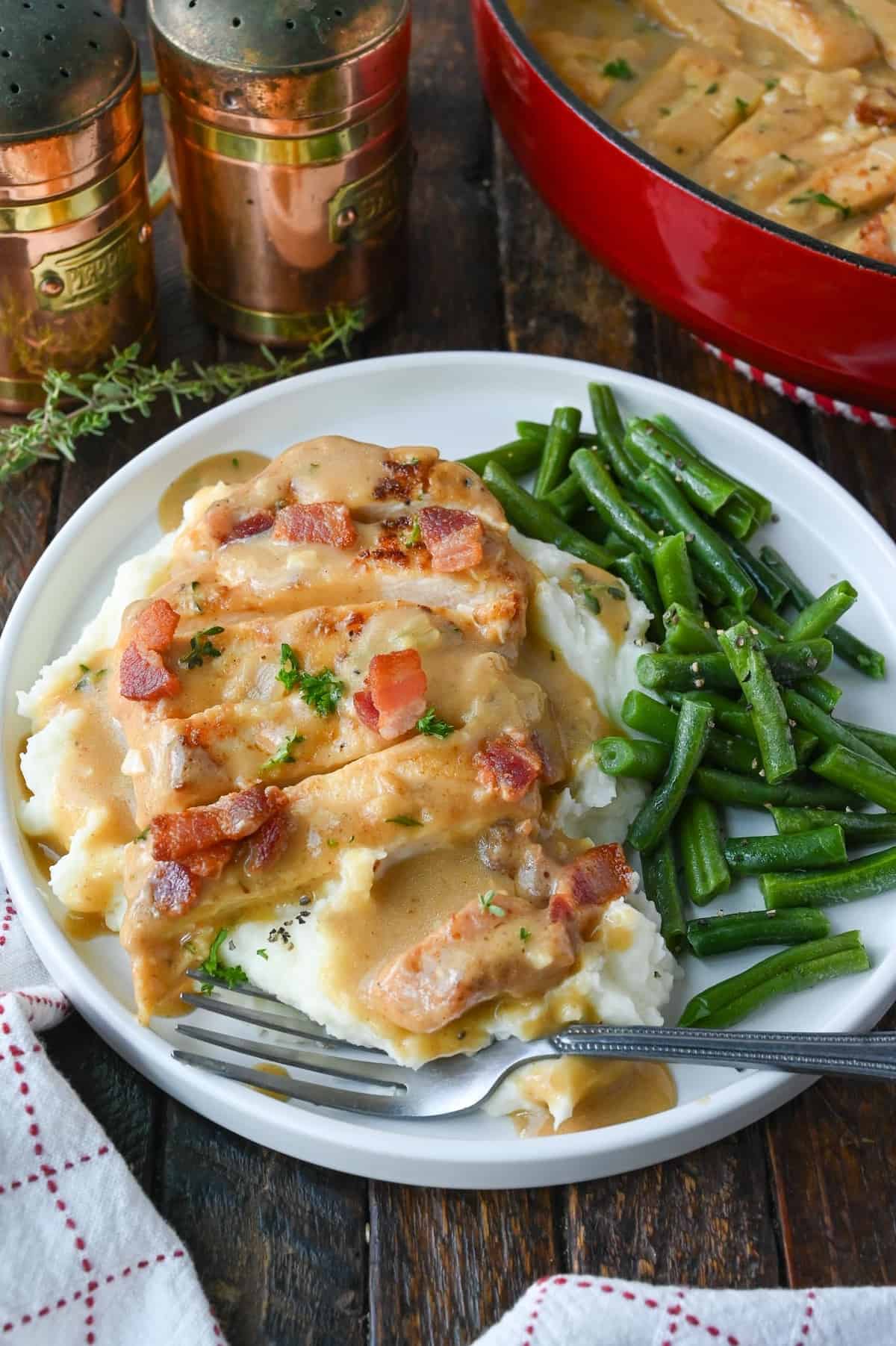 Sliced smothered chicken on top of mashed potatoes with green beans.