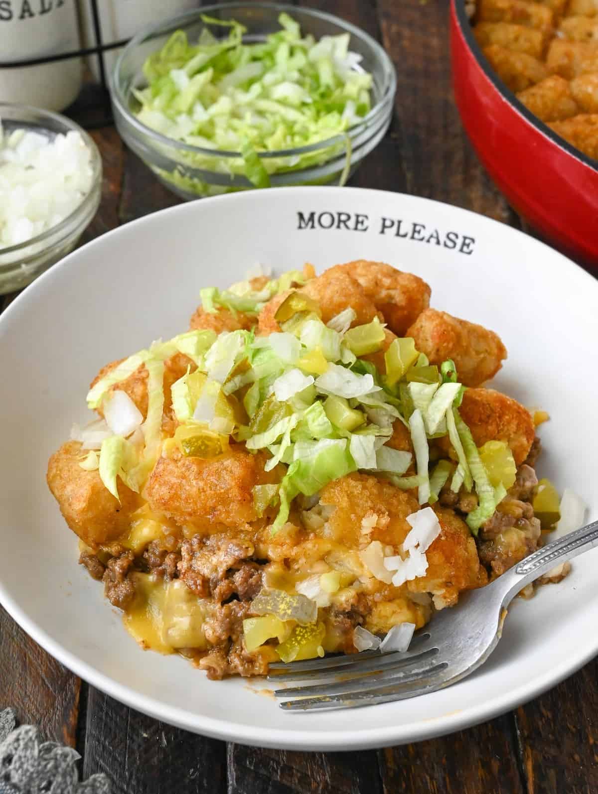 Big mac casserole in a plate with shredded lettuce and diced pickles on top.