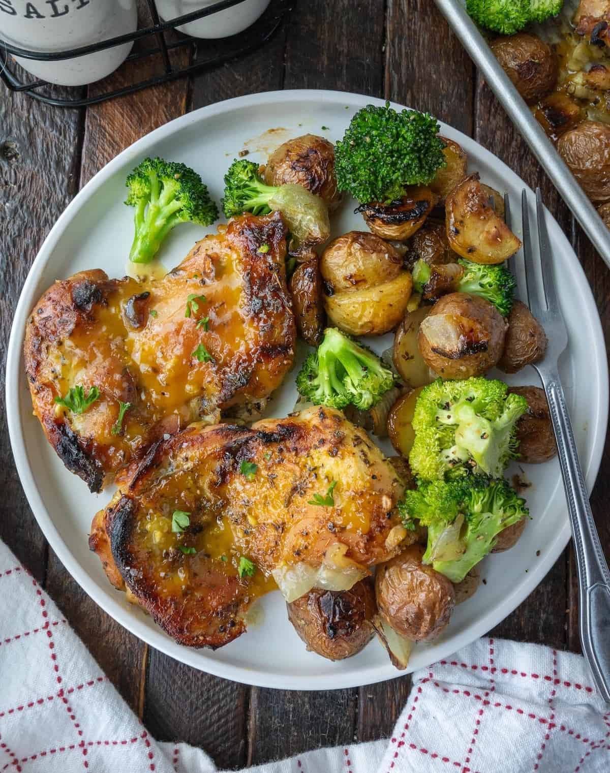 Honey mustard chicken thighs on a plate with broccoli and potatoes.