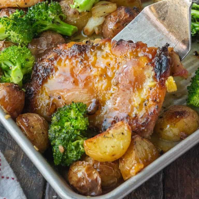 A spatula picking a chicken thigh with potatoes.