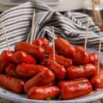 A plate of slow cooker cranberry little smokies with toothpicks sticking out of five of them.