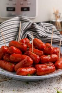 A plate of slow cooker cranberry little smokies with toothpicks sticking out of five of them.