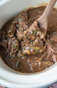 A wooden spoon scooping up some slow cooker round steak in gravy.