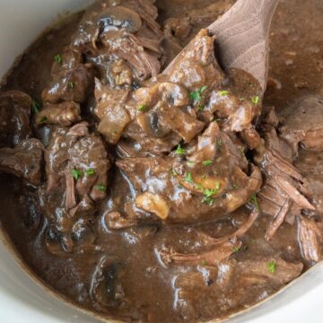 A wooden spoon scooping up some slow cooker round steak in gravy.