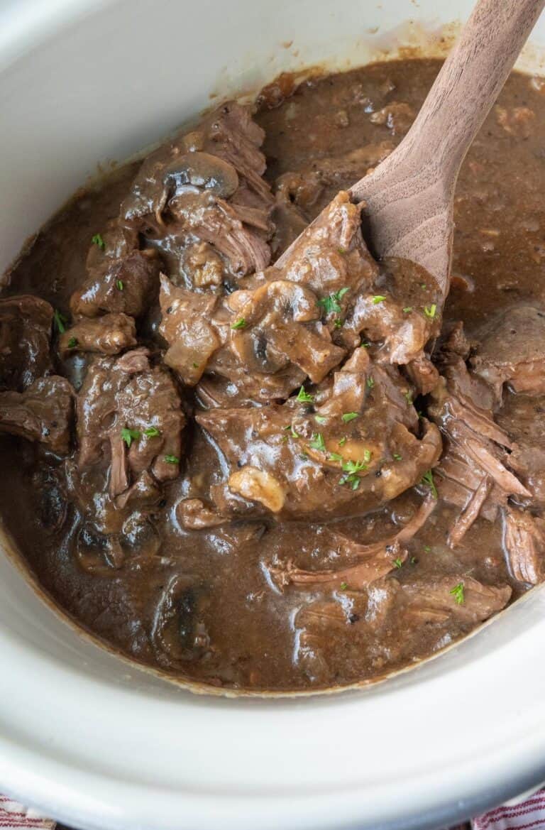 A wooden spoon scooping up some slow cooker round steak in gravy.
