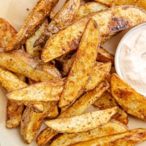 Potato wedges on a platter with a side of dipping sauce.