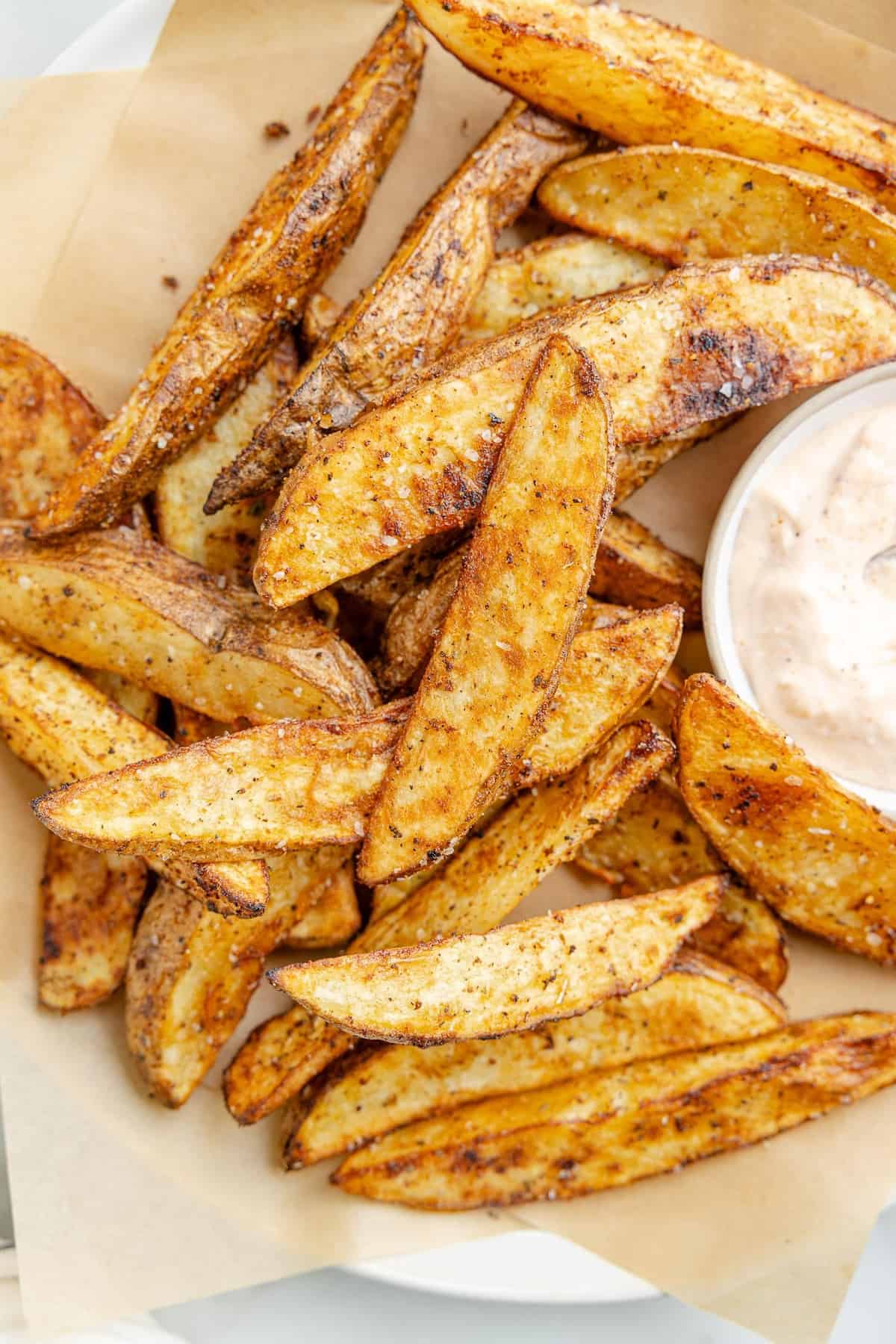 Potato wedges on a platter with a side of dipping sauce.