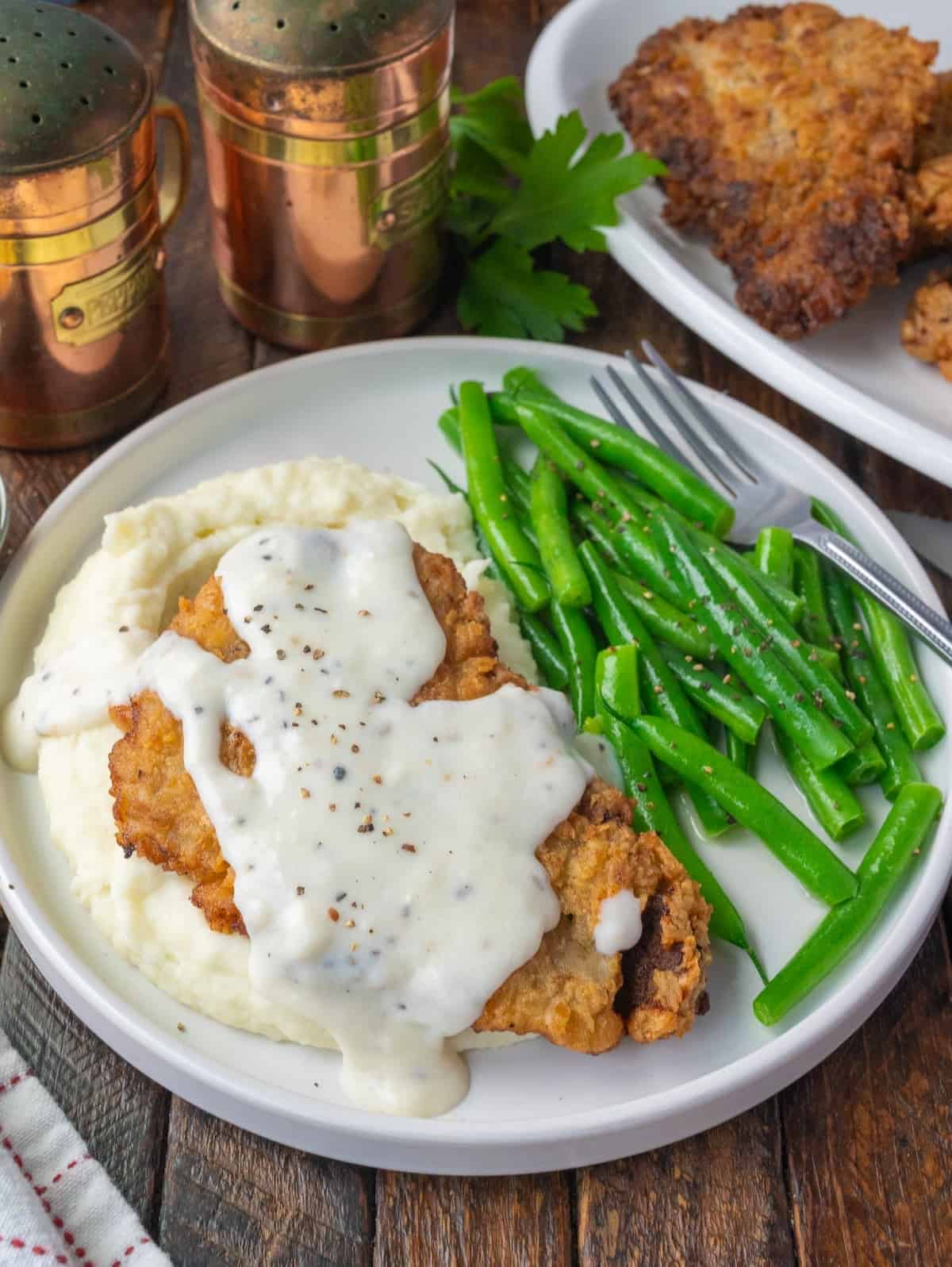 Chicken fried steak with gravy over mashed potatoes with a side of green beans.