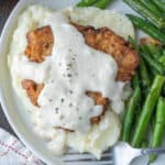 Close up of chicken fried steak with gravy, mashed potatoes, and green beans.