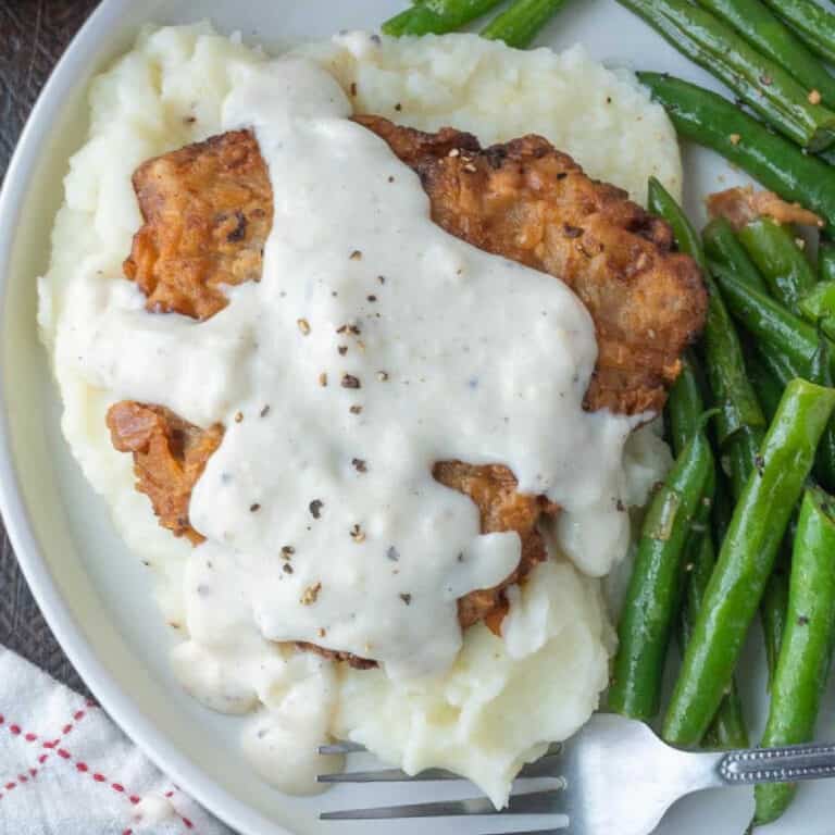 Close up of chicken fried steak with gravy, mashed potatoes, and green beans.