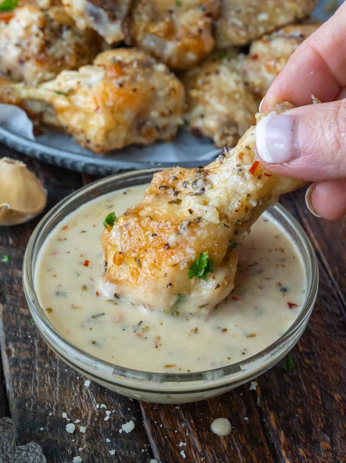 Garlic parmesan chicken wing being dipped into sauce.