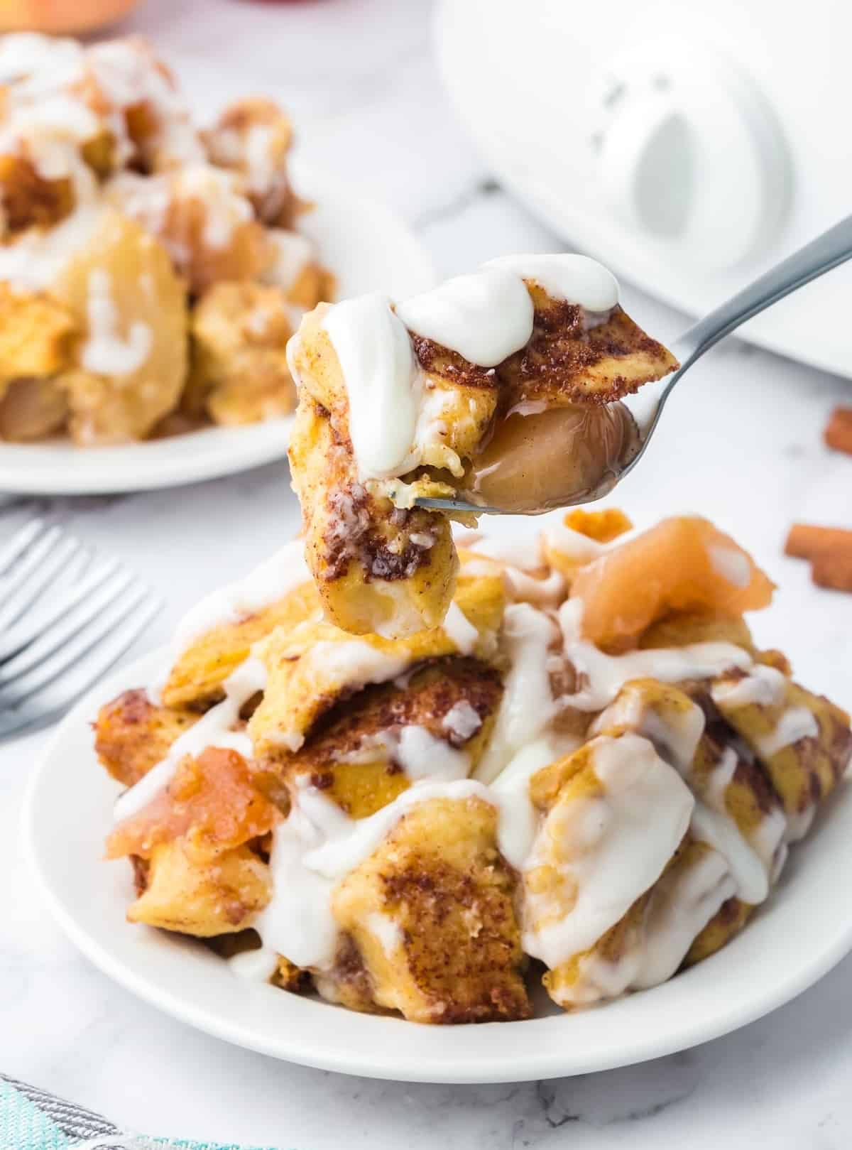 Crockpot cinnamon roll casserole on a plate and a bite picked up with a fork.